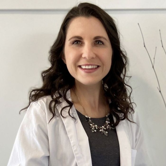 Smiling woman in white lab coat, professional setting.