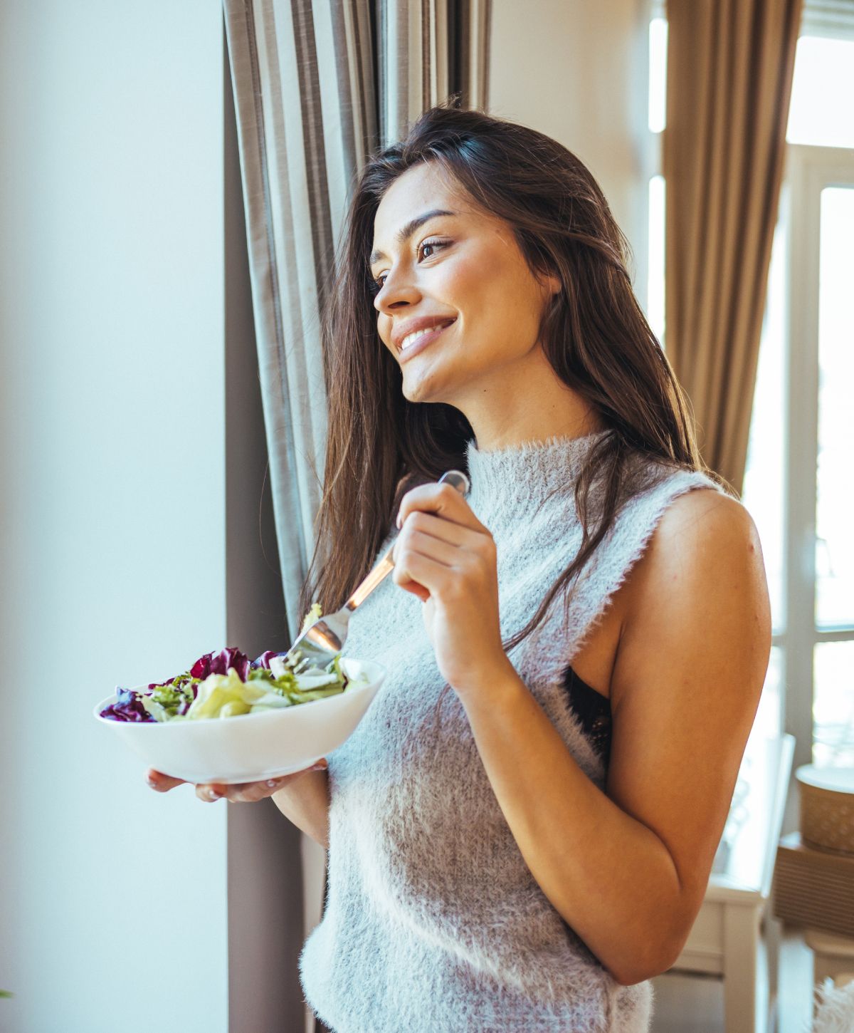 Smiling woman enjoying a healthy salad indoors.