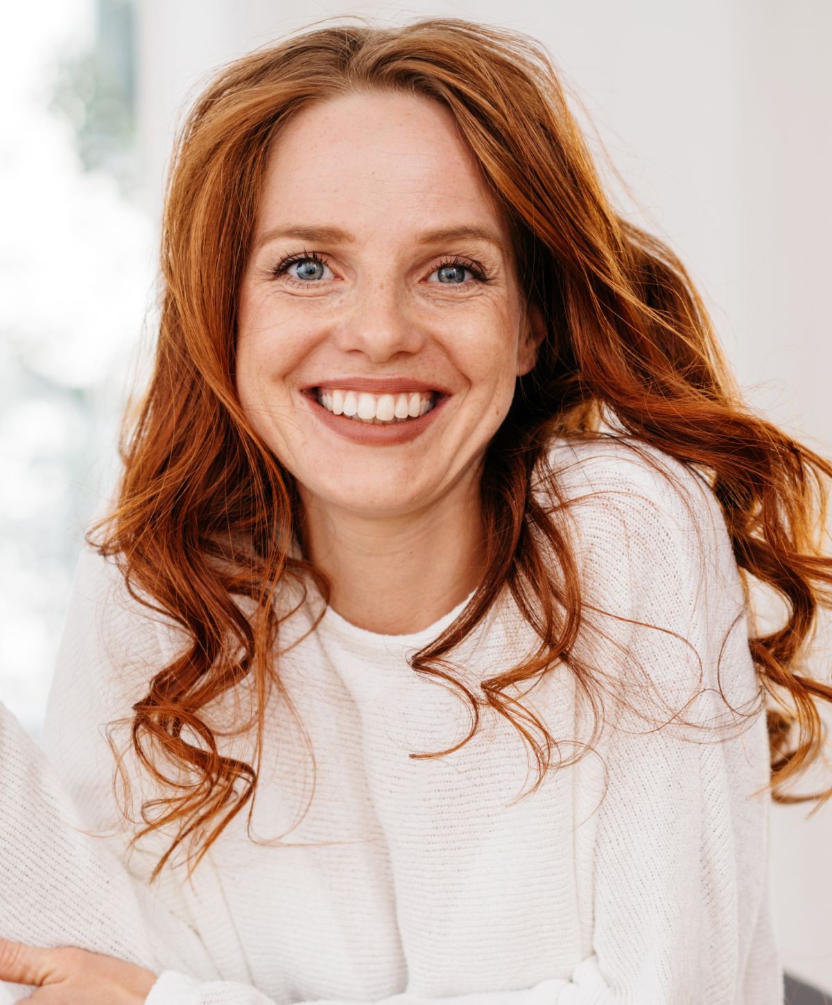 Smiling woman with curly red hair indoors.