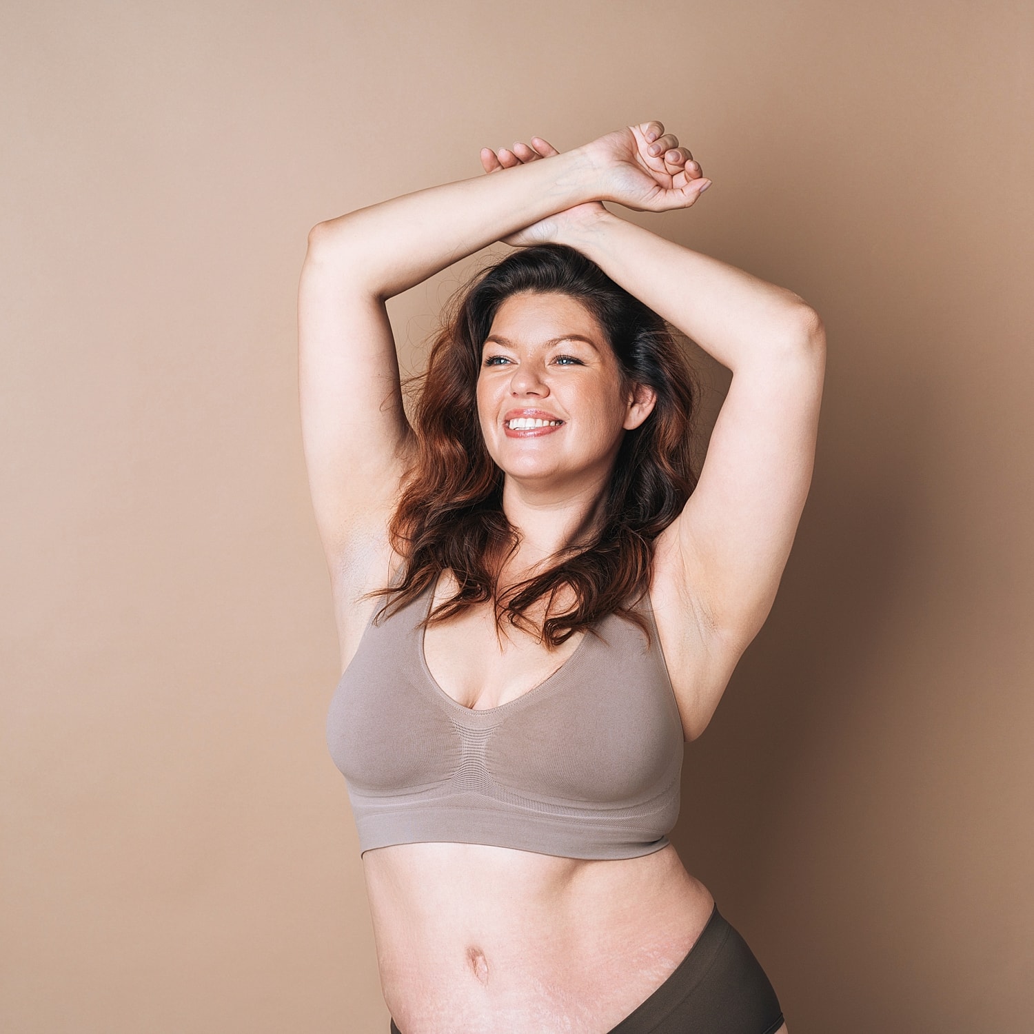 Smiling woman in comfortable lingerie against beige background.