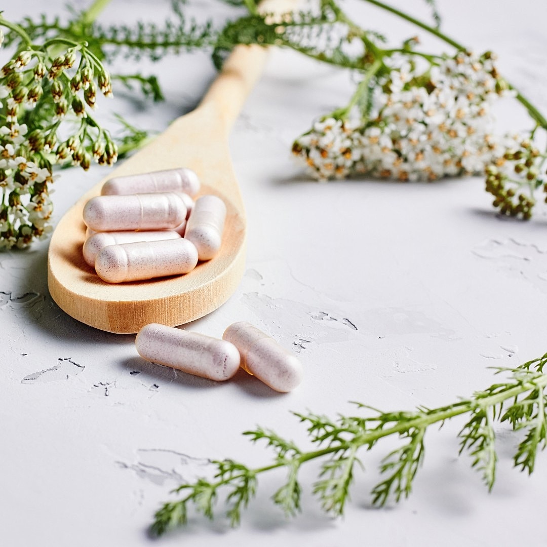 Natural supplements on a wooden spoon with herbs.