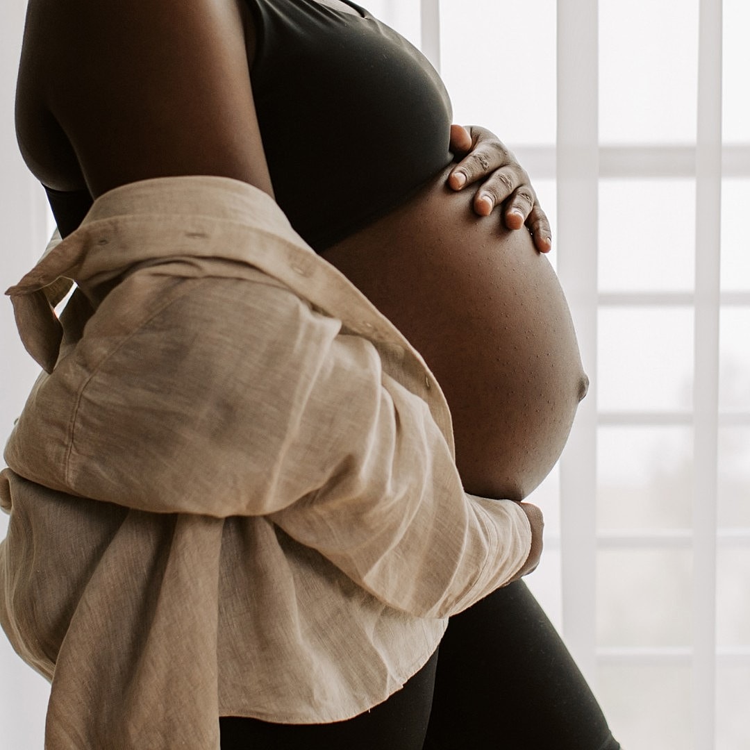 Pregnant person holding belly by window.