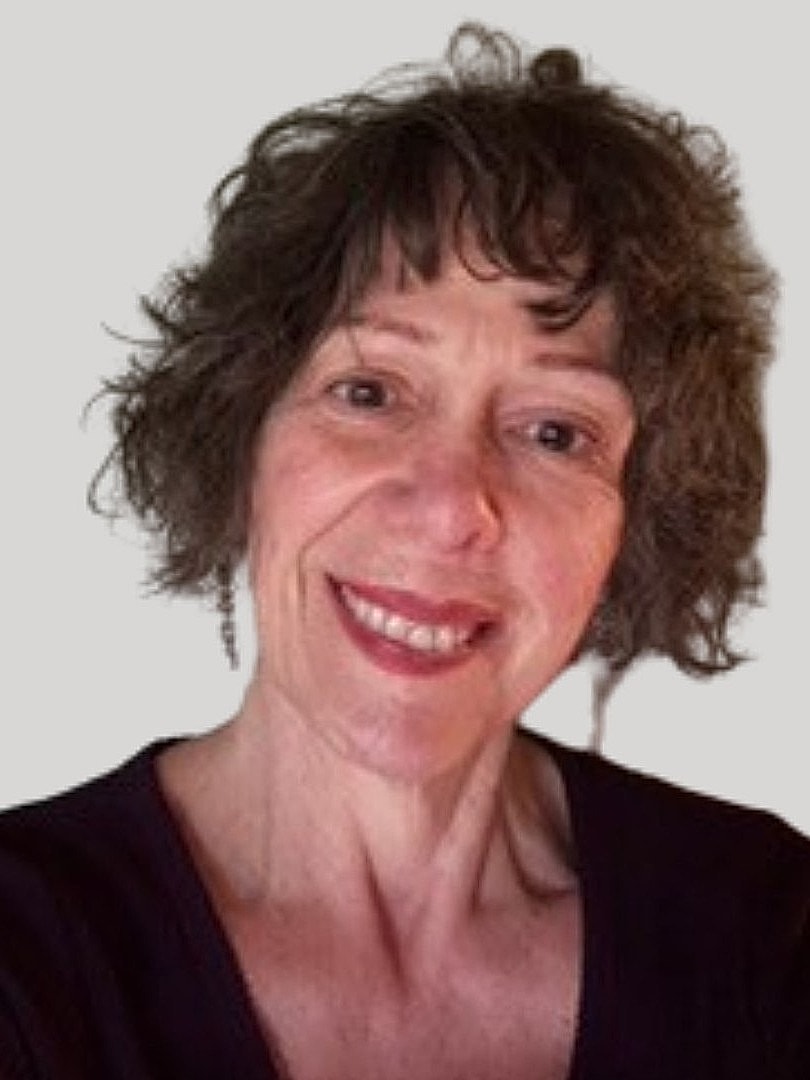 Smiling woman with curly hair against a wall.