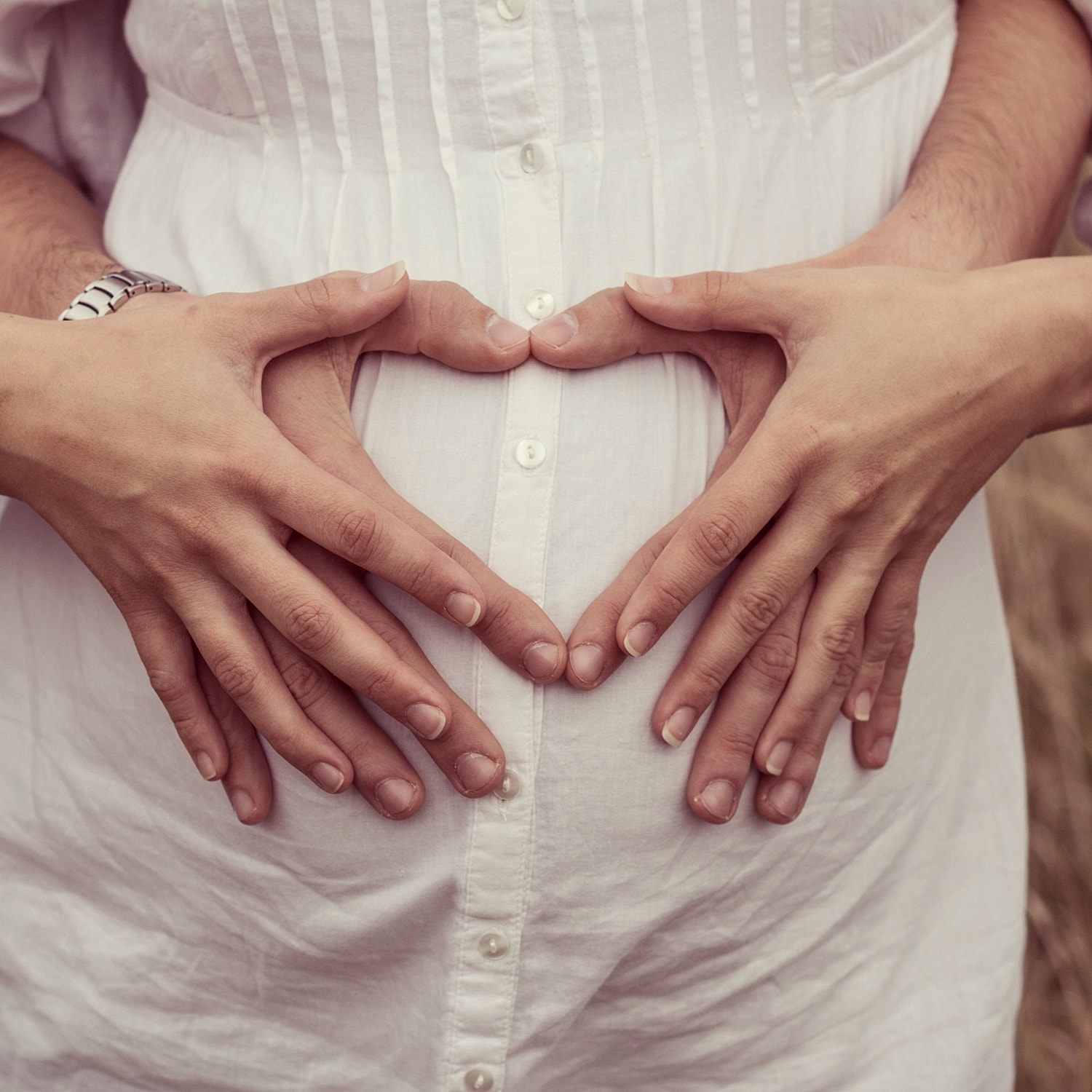 Hands forming heart shape on a pregnant belly.