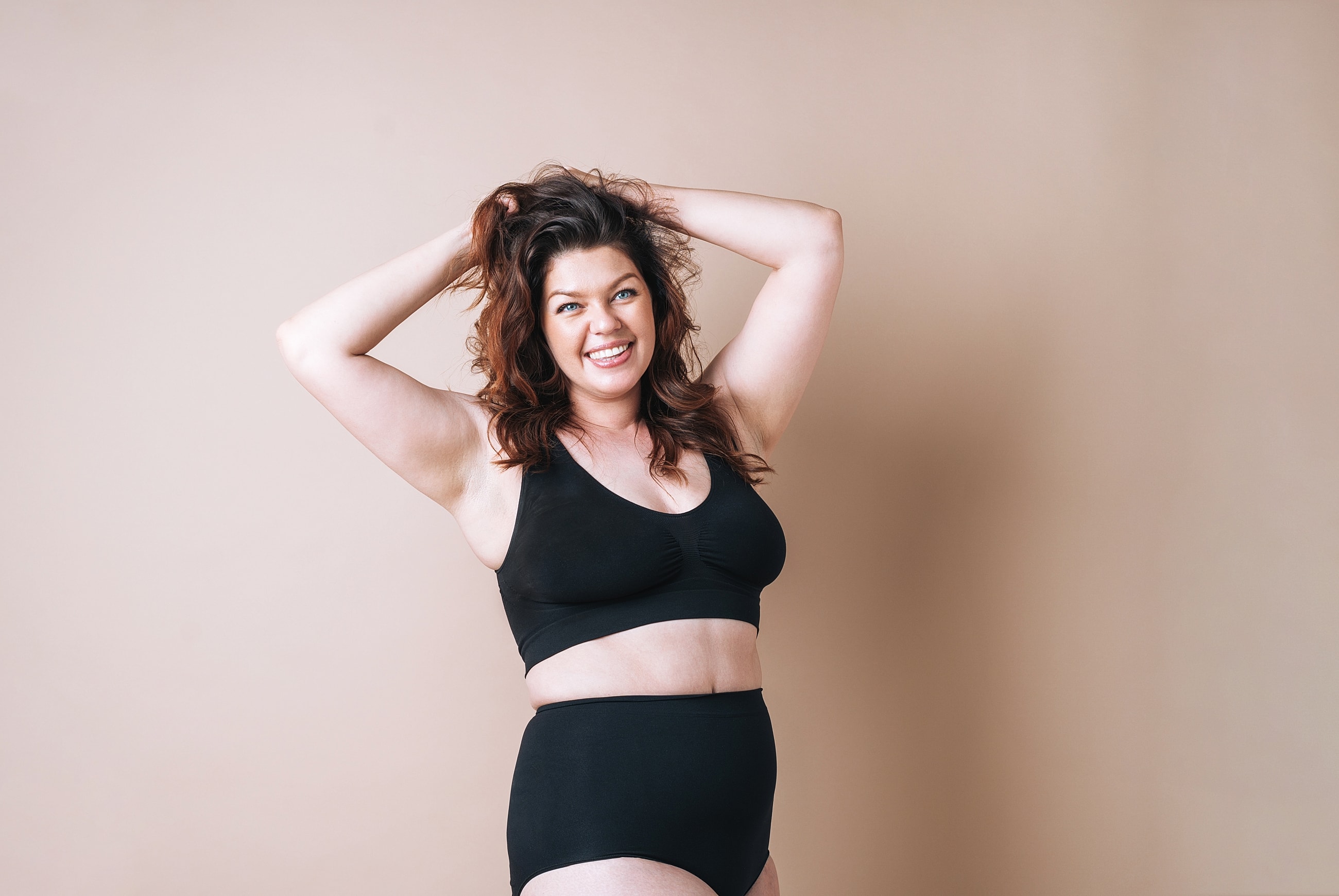 Smiling woman wearing black lingerie against beige background.